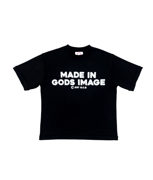 A transparent flat lay of the MUST PREVAIL black 425 GSM heavyweight French Terry inside-out tee. Features 'MADE IN GODS IMAGE' text printed on the front, an oversized boxy fit, inside-out stitching details, and distressed hems for a technical streetwear aesthetic.