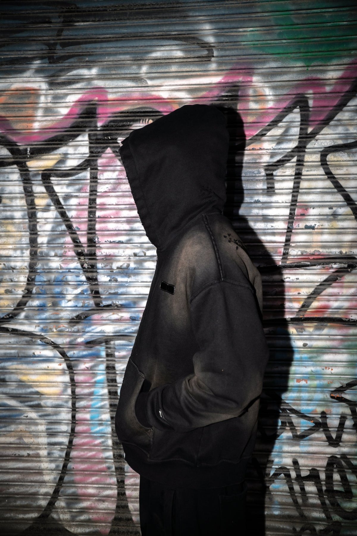 On-body closeup of the black 500 GSM heavyweight French Terry full-zip hoodie styled by MUST PREVAIL. This Y2K-inspired garment features a cropped-drop shoulder fit, oversized deep-V hood, and YKK zipper. Highlights include a two-tone sand-blast vintage aesthetic with micro-distressing and sewn-on adhesive labeling.