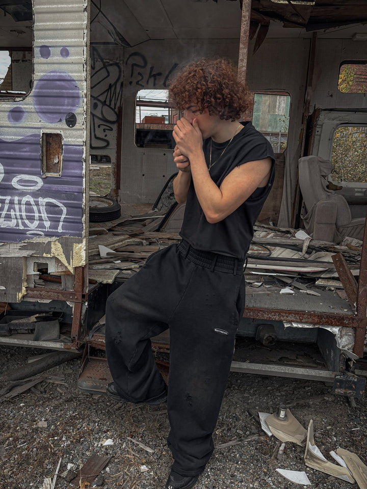 On-body closeup of the black 500 GSM French Terry oversized baggy sweatpants styled by MUST PREVAIL. The image showcases the unique triple waistband with belt loops, wide-leg fit, and two-tone sand-blast distressing. Features micro-distressing, double-front pockets, and sewn-on adhesive labeling on a heavy-weight Y2K-inspired silhouette.
