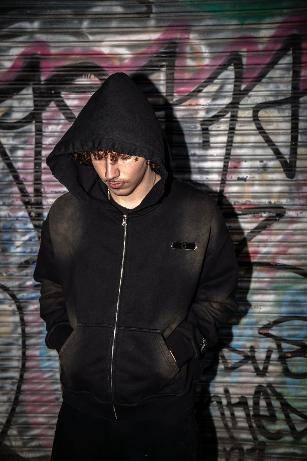 Front-facing on-body view of the black 500 GSM French Terry full-zip hoodie styled by MUST PREVAIL. This Y2K-inspired garment features a cropped-drop shoulder, oversized deep-V hood, and YKK zipper. Shows the two-tone sand-blast vintage aesthetic with micro-distressing and sewn-on adhesive labeling.