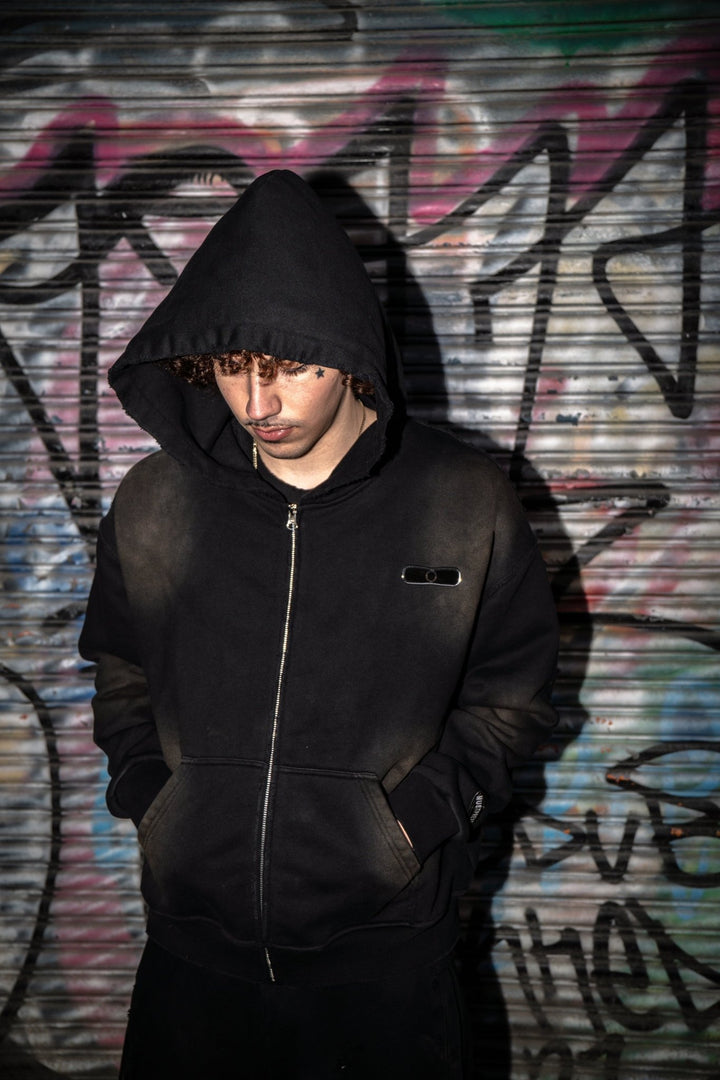 Front-facing on-body view of the black 500 GSM French Terry full-zip hoodie styled by MUST PREVAIL. This Y2K-inspired garment features a cropped-drop shoulder, oversized deep-V hood, and YKK zipper. Shows the two-tone sand-blast vintage aesthetic with micro-distressing and sewn-on adhesive labeling.