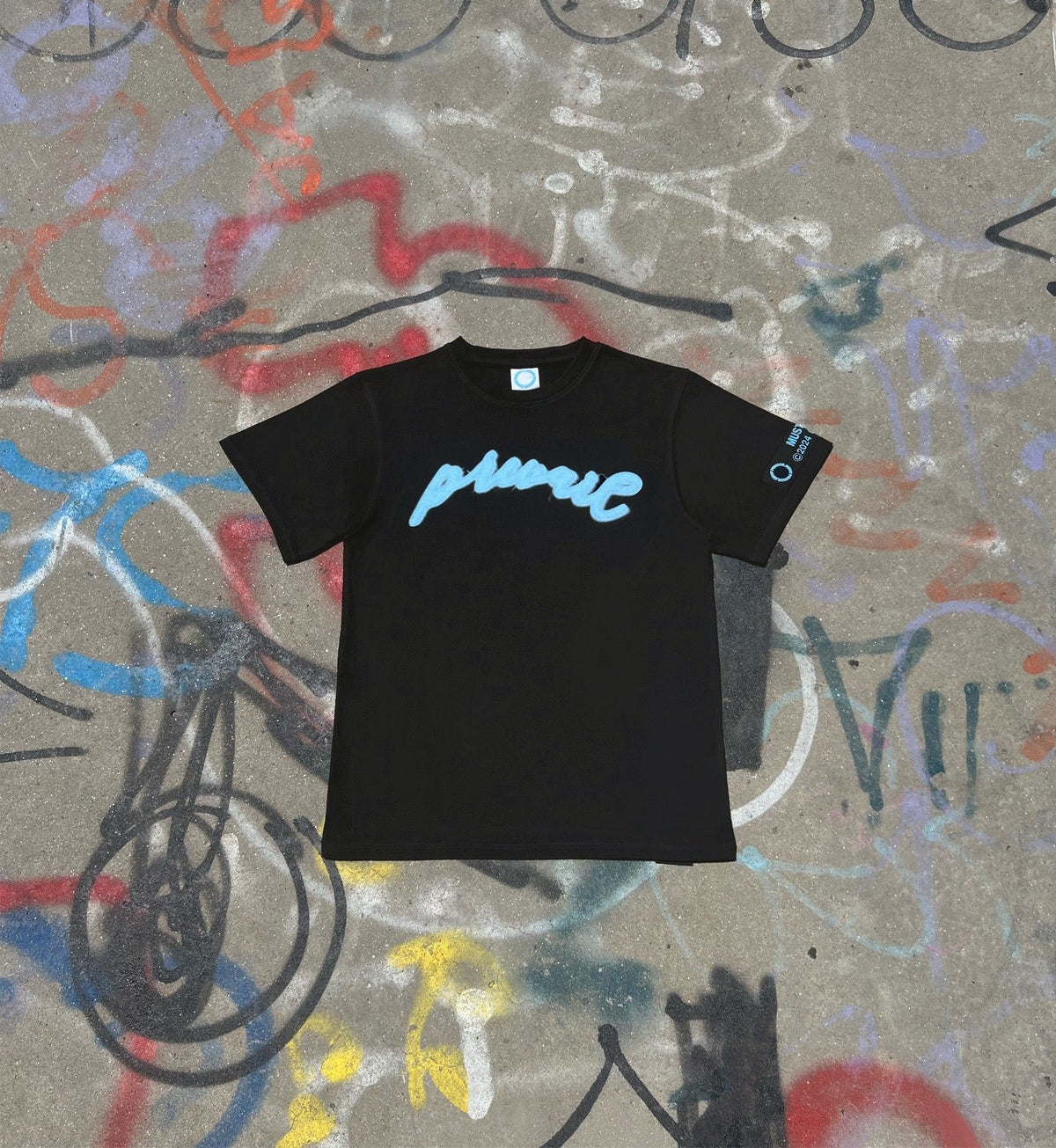 "A flat lay of the MUST PREVAIL 'Prevail' statement tee in heather grey on a graffiti-covered concrete surface. This shot showcases the vibrant blue 'PREVAIL' DTG print and the oversized boxy silhouette against an industrial, urban backdrop. Highlights the heavyweight cotton texture and deconstructed streetwear aesthetic of the collection.